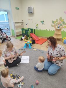 Dzieci z opiekunkami w trakcie zajęć z wykorzystaniem instrumentu ukulele.