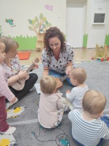 Dzieci z opiekunkami w trakcie zajęć z wykorzystaniem instrumentu ukulele.
