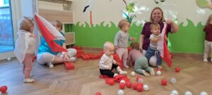 Ciocia z dziećmi bawi się białymi i czerwonymi chustami.