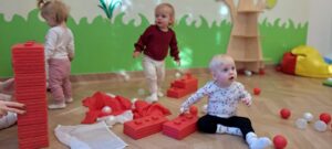 Ciocia buduje z dziećmi wieżę z dużych czerwonych klocków.