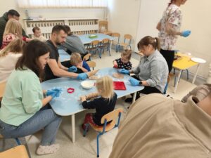 Dzieci wraz z rodzicami przy stolikach wałkują oraz wykrawają pierniczki