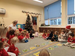 Dzieci siedzą na dywanie a Mikołaj wchodzi do sali