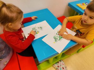 Dzieci naklejają bombkę z plasteliny na namalowaną choinkę
