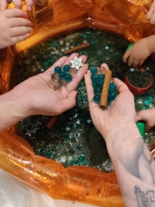 Zdjęcie rąk opiekunek pokazujących masę- kulki hydrożelowe, chia, plastikowe śnieżynki i cynamon