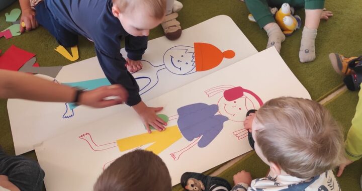 Dzieci wyklejają ubranka zimowe na postaciach dziewczynki i chłopczyka.