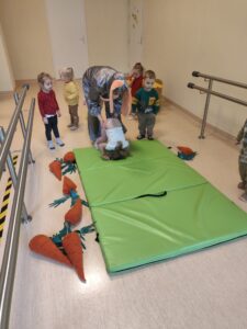 Dzieci z pomocą cioci robią fikołki na materacu