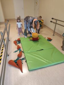 Dzieci z pomocą cioci robią fikołki na materacu