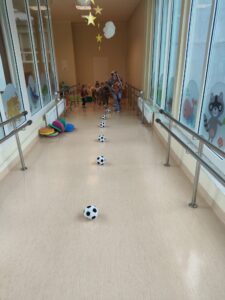 Dzieci i ciocia w stroju Królika trzymając pluszowe marchewki pokonują slalom z piłek