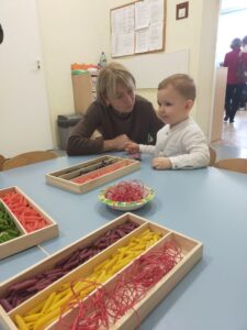 Dzieci wraz z dziadkami robią korale z kolorowego makaronu