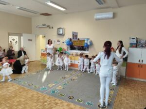 Dzieci ubrane całe na biało tańczą na dywanie