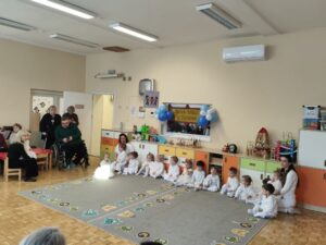 Dzieci ubrane całe na biało siedzą na dywanie