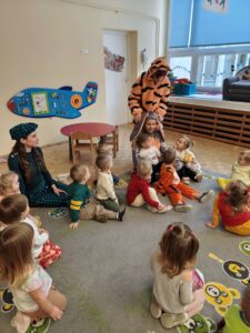 Dzieci siedzą na dywanie a ciocia w stroju Tygryska prezentuje postać cioci rozebranej za Królika