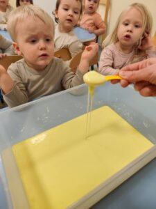 Dzieci patrzą jak masa plastyczną rozlewa się z łyżeczki