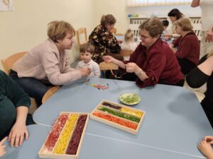 Dzieci wraz z dziadkami robią korale z kolorowego makaronu