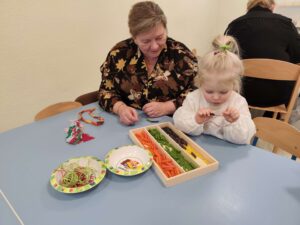 Dzieci wraz z dziadkami robią korale z kolorowego makaronu