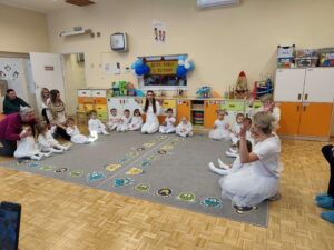 Dzieci w białych strojach siedzą na dywanie