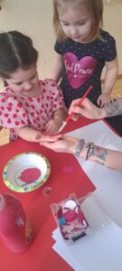 Ciocia maluje dziewczynce dłoń różową farbą