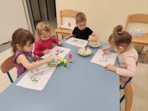 Dzieci wyklejają szablon maski kolorowymi ozdobami