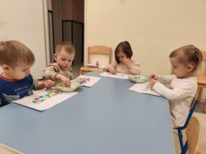 Dzieci wyklejają szablon maski kolorowymi ozdobami