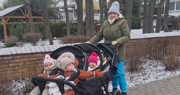 Opiekunka żłobka prowadząca wieloosobowy wózek spacerowy z dziećmi podczas zimowego spaceru na terenie placówki