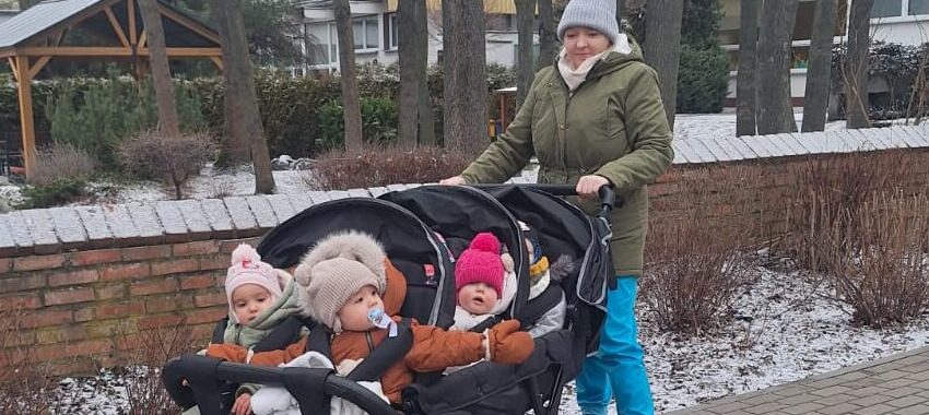 Opiekunka żłobka prowadząca wieloosobowy wózek spacerowy z dziećmi podczas zimowego spaceru na terenie placówki