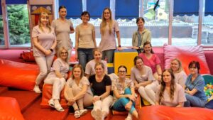 Grupa opiekunów żłobka siedzących i stojących w sali zabaw, po zakończonym szkoleniu dotyczącym współpracy z rodzicami na rzecz dziecka