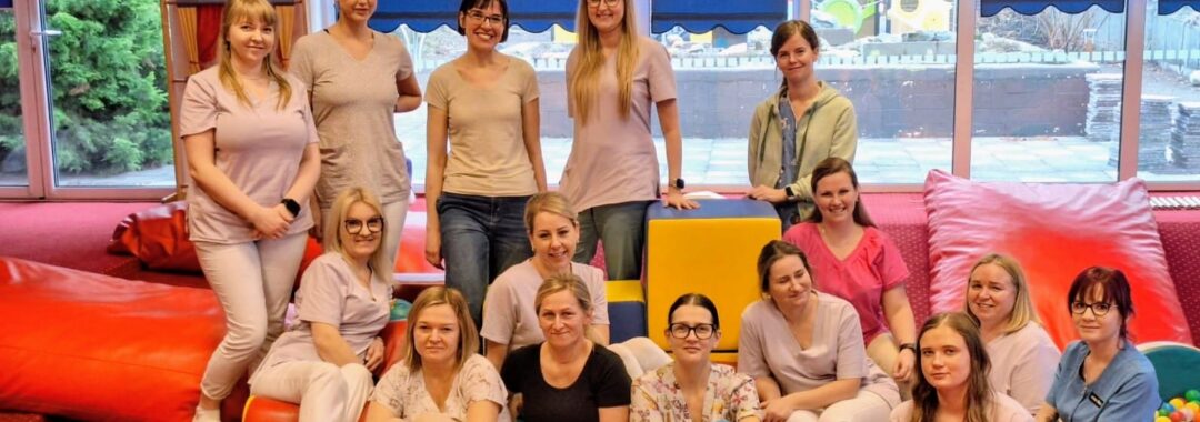 Grupa opiekunów żłobka siedzących i stojących w sali zabaw, po zakończonym szkoleniu dotyczącym współpracy z rodzicami na rzecz dziecka