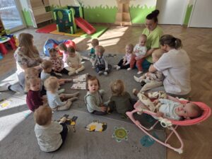 Dzieci siedzą na dywanie z ciociami. wspólnie rozmawiają na temat tego, co jest dobre dla zębów a co szkodzi.