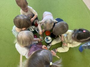 Dzieci za pomocą drewnianych szczypiec wkładają kolorowe pompony do odpowiednich pojemników