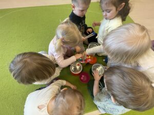Dzieci za pomocą drewnianych szczypiec wkładają kolorowe pompony do odpowiednich pojemników