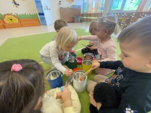 Dzieci za pomocą drewnianych szczypiec wkładają kolorowe pompony do odpowiednich pojemników