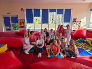 Zespół opiekunów żłobka podczas szkolenia prowadzonego przez fizjoterapeutkę – wspólne zdjęcie uczestników w sali zabaw.