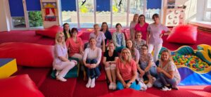 Zespół opiekunów żłobka podczas szkolenia prowadzonego przez fizjoterapeutkę – wspólne zdjęcie uczestników w sali zabaw.
