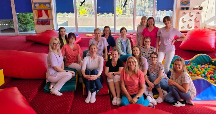 Zespół opiekunów żłobka podczas szkolenia prowadzonego przez fizjoterapeutkę – wspólne zdjęcie uczestników w sali zabaw.