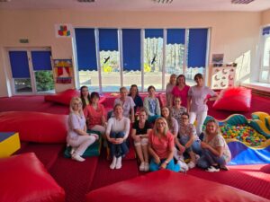 Zespół opiekunów żłobka podczas szkolenia prowadzonego przez fizjoterapeutkę – wspólne zdjęcie uczestników w sali zabaw.