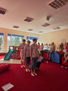 Część praktyczna szkolenia – fizjoterapeutka pokazuje opiekunom prawidłowe ułożenie ciała i postawę podczas pracy z dzieckiem.