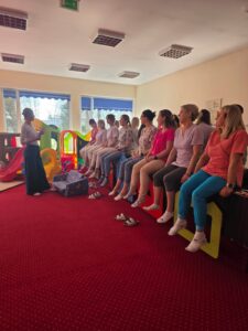 Część praktyczna szkolenia – fizjoterapeutka pokazuje opiekunom prawidłowe ułożenie ciała i postawę podczas pracy z dzieckiem.