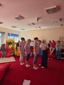 Część praktyczna szkolenia – fizjoterapeutka pokazuje opiekunom prawidłowe ułożenie ciała i postawę podczas pracy z dzieckiem.