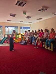 Część praktyczna szkolenia – fizjoterapeutka pokazuje opiekunom prawidłowe ułożenie ciała i postawę podczas pracy z dzieckiem.