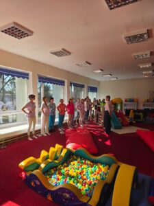 Część praktyczna szkolenia – fizjoterapeutka pokazuje opiekunom prawidłowe ułożenie ciała i postawę podczas pracy z dzieckiem.