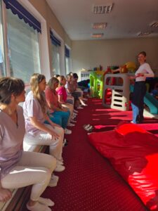 Część praktyczna szkolenia – fizjoterapeutka pokazuje opiekunom prawidłowe ułożenie ciała i postawę podczas pracy z dzieckiem.