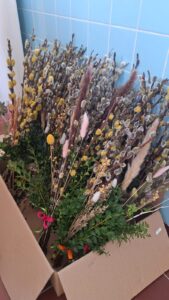 Gotowe i przygotowywane palmy wielkanocne ułożone na stole podczas pracy zespołowej.