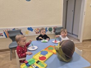 Dzieci malują farbami papierowy talerzyk, który będzie skorupą ślimaka. Dziewczynka ogląda dużego ślimaka.