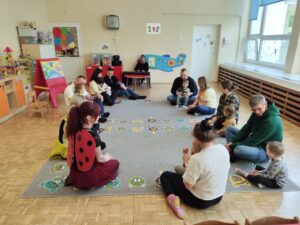 Dzieci wraz z rodzicami siedzą na dywanie