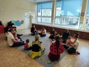 Dzieci wraz z rodzicami siedzą na dywanie