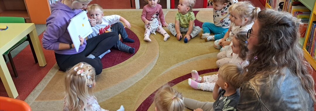 Dzieci słuchają pani z biblioteki która czyta im książeczki