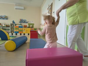 Dziewczynka skacze z piankowej kotki. Ciocia jej pomaga.