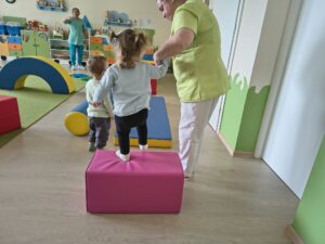 Ciocia pomaga dziecku bezpiecznie zeskoczyć z piankowej ostki.