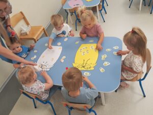 Dzieci przyklejają na słoiczki warzywa i owoce tworząc jesienne przetwory