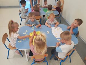 Dzieci przyklejają na słoiczki warzywa i owoce tworząc jesienne przetwory